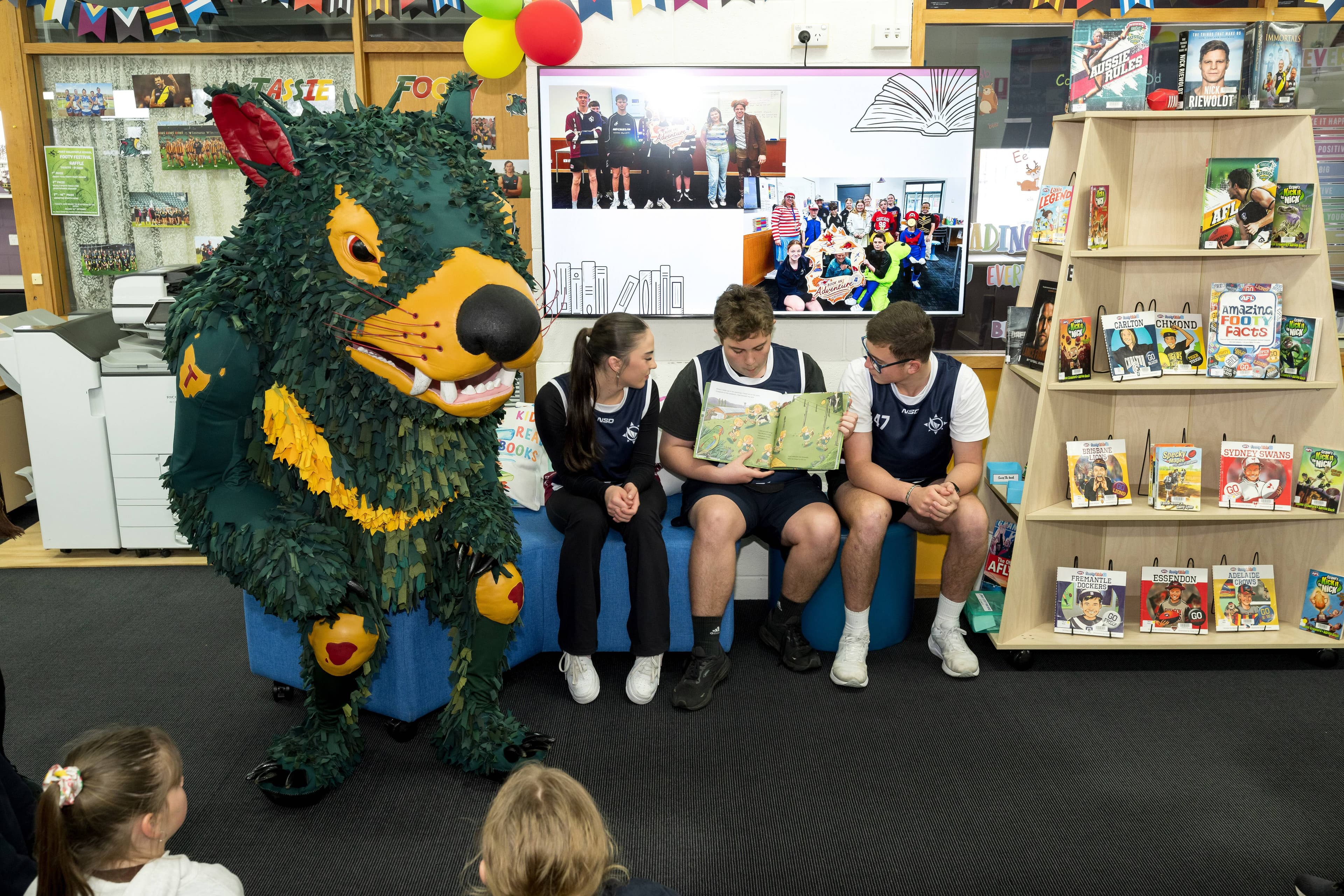 Keeley Trudgeon, Maverick Watson, and Tajh Wilson read to students in the library
at Port Dalrymple footy colours day, the day before the AFL Grand Final.